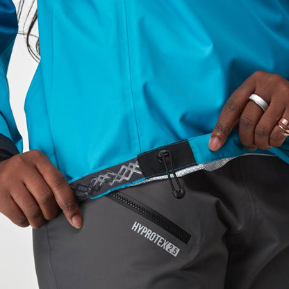 A person adjusts the hem of an NRS Endurance Splash Jacket - Women's in blue with a cord and toggle, paired with dark pants labeled "Hyprotek 2.5.