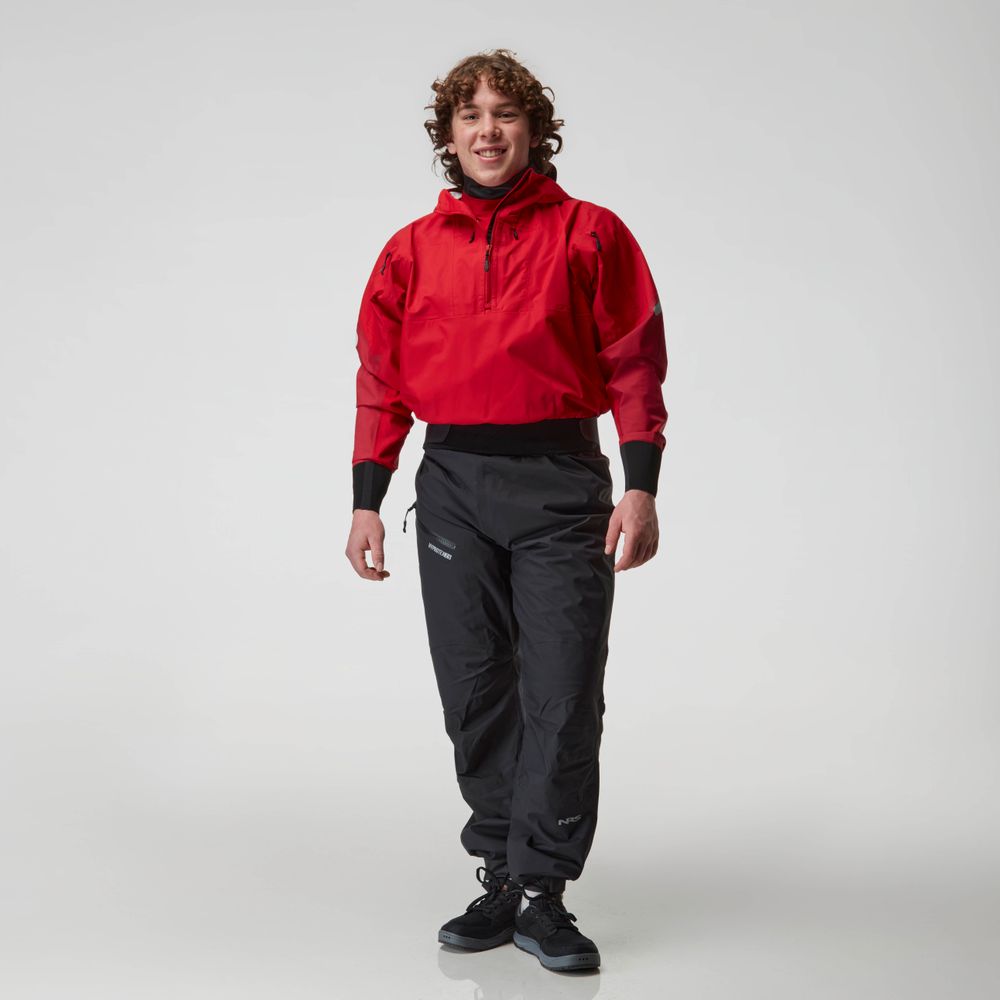 A person stands against a white background wearing a red waterproof jacket and black NRS Endurance Splash Pant - Men's, made with waterproof breathable HyproTex fabric, paired with black shoes.