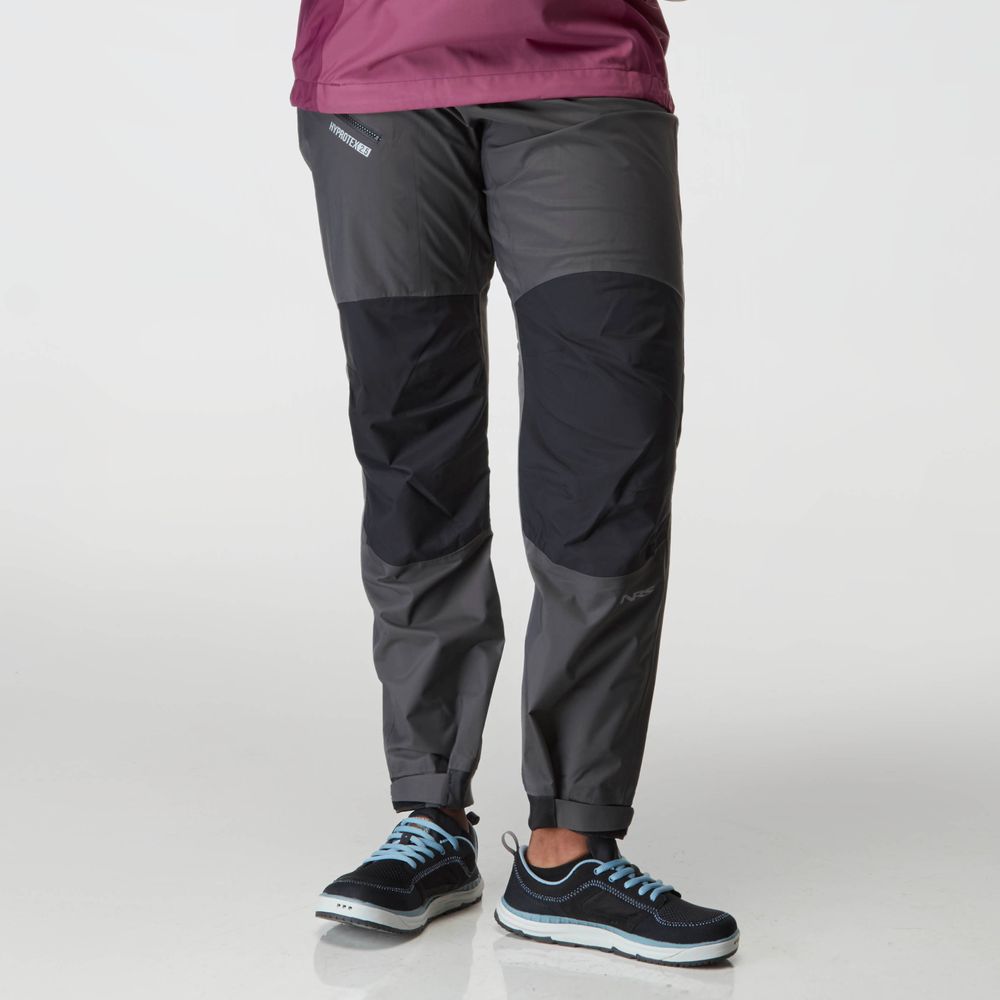Dressed in NRS Endurance Splash Pant - Women's, featuring gray and black HyproTex material, teamed with black sneakers accented in blue, one remains prepared for any challenge.