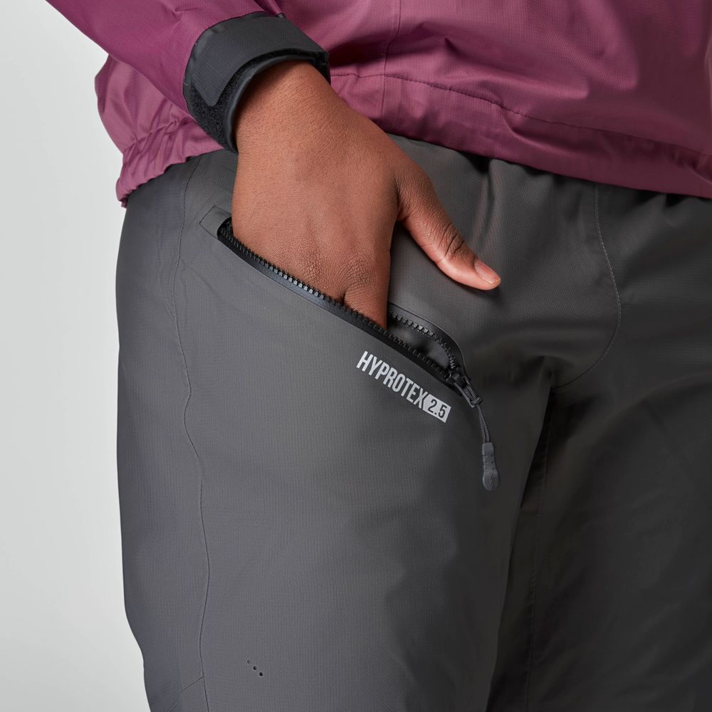 Close-up of a person wearing NRS Endurance Splash Pant - Women's in gray, with a visible "HYPROTEX 2.5" zip pocket and a black wristband. The pants feature reinforced seat and knees for durability and extra protection against the elements.