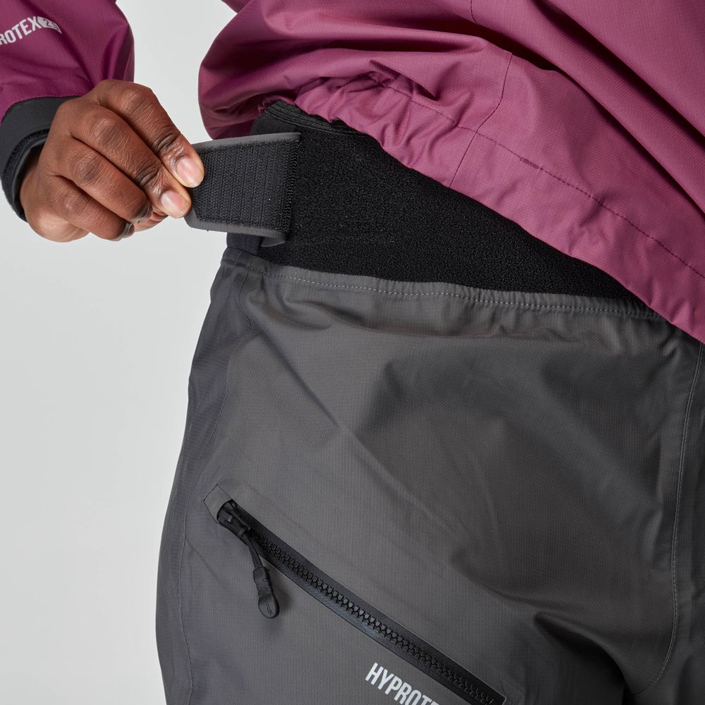 She adjusted the velcro strap of a gray jacket with a zippered pocket and paired it with NRS Endurance Splash Pant - Women's, crafted from HyproTex material, perfectly complementing her plum-colored outer layer.
