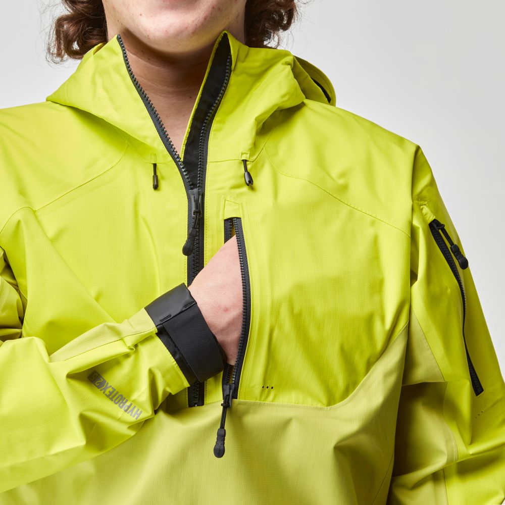 A person adjusts a pocket on their High Tide Jacket - Men's in bright yellow-green, designed by NRS, featuring multiple zippers.