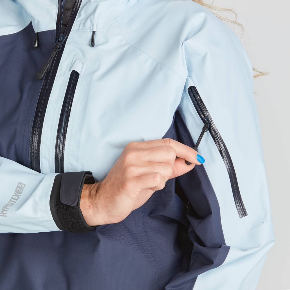 A person zips a pocket on the sleeve of an NRS High Tide Jacket - Women's in light blue and dark blue, wearing a smartwatch.