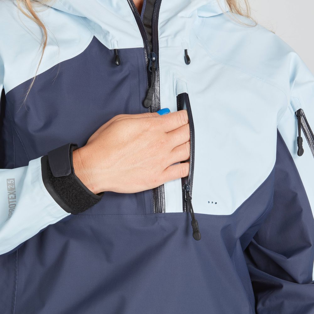 A person in the NRS High Tide Jacket for women, featuring a blue and light blue paddler's cut design, adjusts the zipper on the chest pocket.