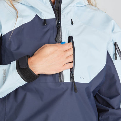 A person in the NRS High Tide Jacket for women, featuring a blue and light blue paddler's cut design, adjusts the zipper on the chest pocket.