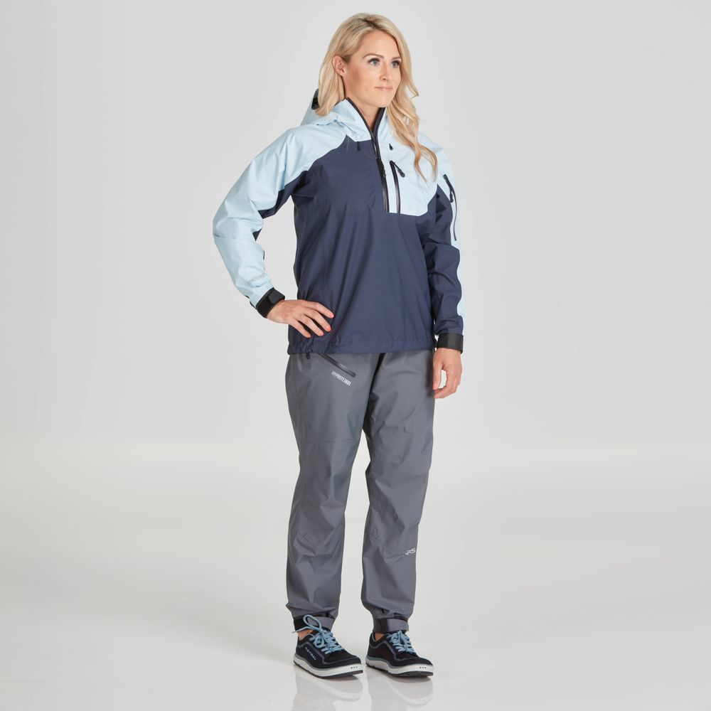 A person wearing the NRS High Tide Jacket - Women's, gray pants, and sneakers stands on a plain background with hands on hips.