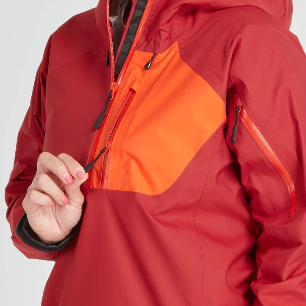 A woman wearing the NRS High Tide Jacket in red and orange adjusts the front zipper. This waterproof jacket provides breathable protection, features an adjustable hood, and is ideal for unpredictable weather.