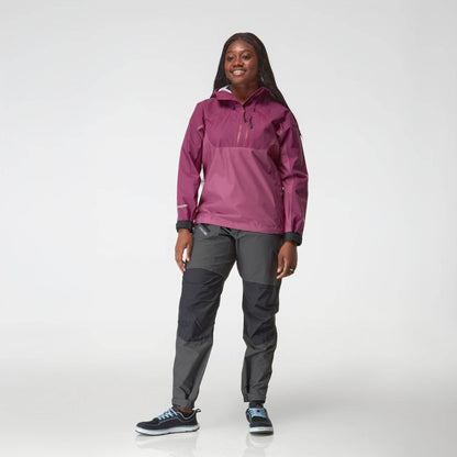 A person smiles against a plain background, modeling the NRS High Tide Jacket for women—a chic purple splash jacket featuring an adjustable hood—perfectly matched with gray pants.