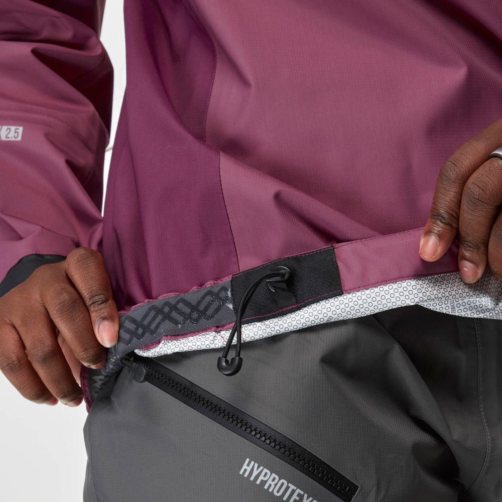 A person adjusts the waistband drawcord of the NRS High Tide Jacket - Women's, revealing its mesh lining and a zippered pocket labeled "HYPTOTEX 2.5" on grey pants.