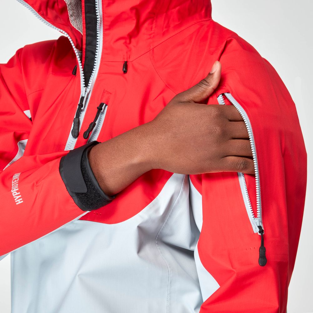 A person adjusts the sleeve zipper on the NRS High Tide Jacket - Women's, a red and gray waterproof splash jacket designed for breathable protection in any weather.