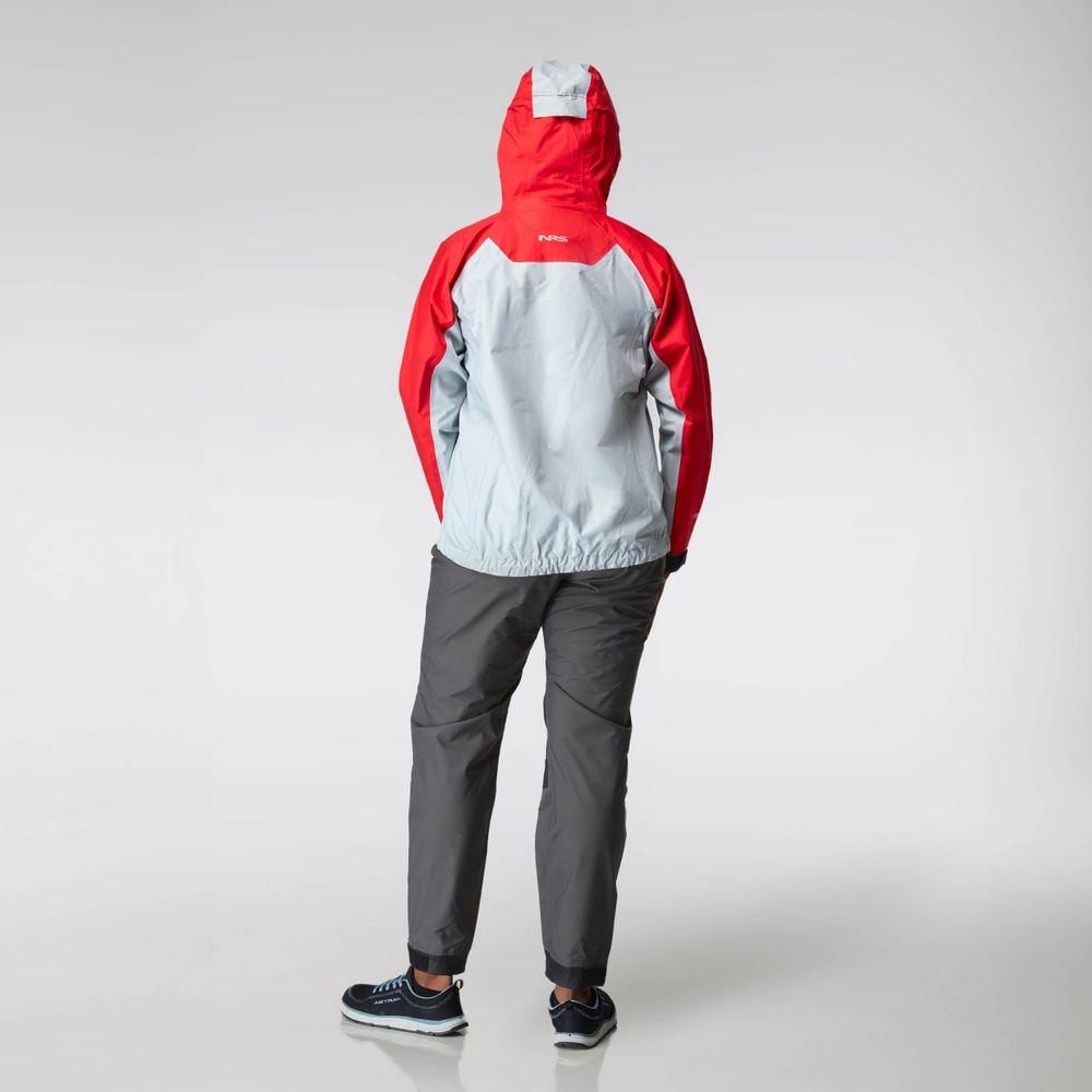 Clad in the NRS High Tide Jacket - Women's in red and gray with its hood up, a person stands with hands in pockets, facing away, paired with gray pants and black sneakers.