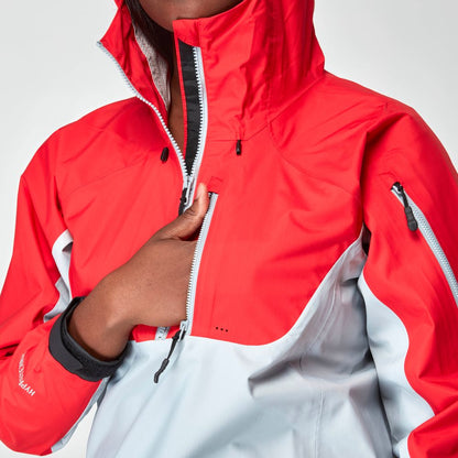 She's wearing the NRS High Tide Jacket in red and gray, confidently gripping the zipper of its waterproof design with a high collar.