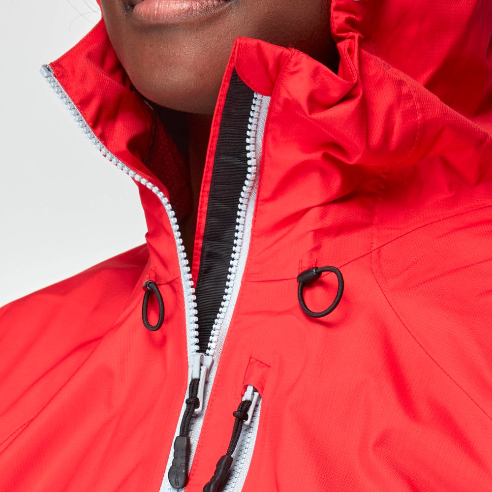 A close-up showcases a person in an NRS Women's High Tide Jacket, boasting a high-collared red waterproof design with stylish black and white zippers. The adjustable hood adds versatility, and its breathable protection guarantees comfort in various conditions.