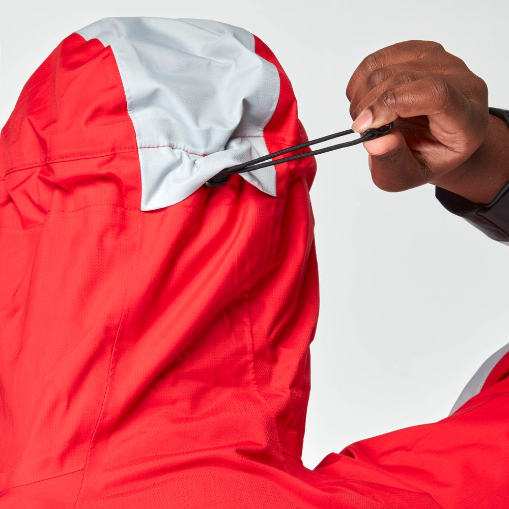 A person tightens the drawstring on the hood of a red and gray NRS High Tide Jacket for women.
