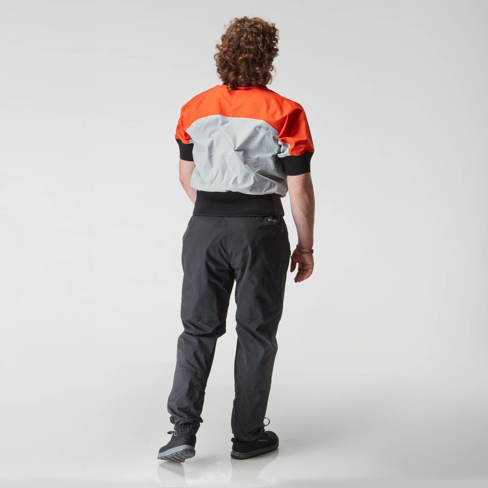 A person with curly hair faces away, wearing an NRS Stratos Short Sleeve Paddling Jacket in red and gray with neoprene neck and arm seals, black pants, and sneakers against a plain white background.