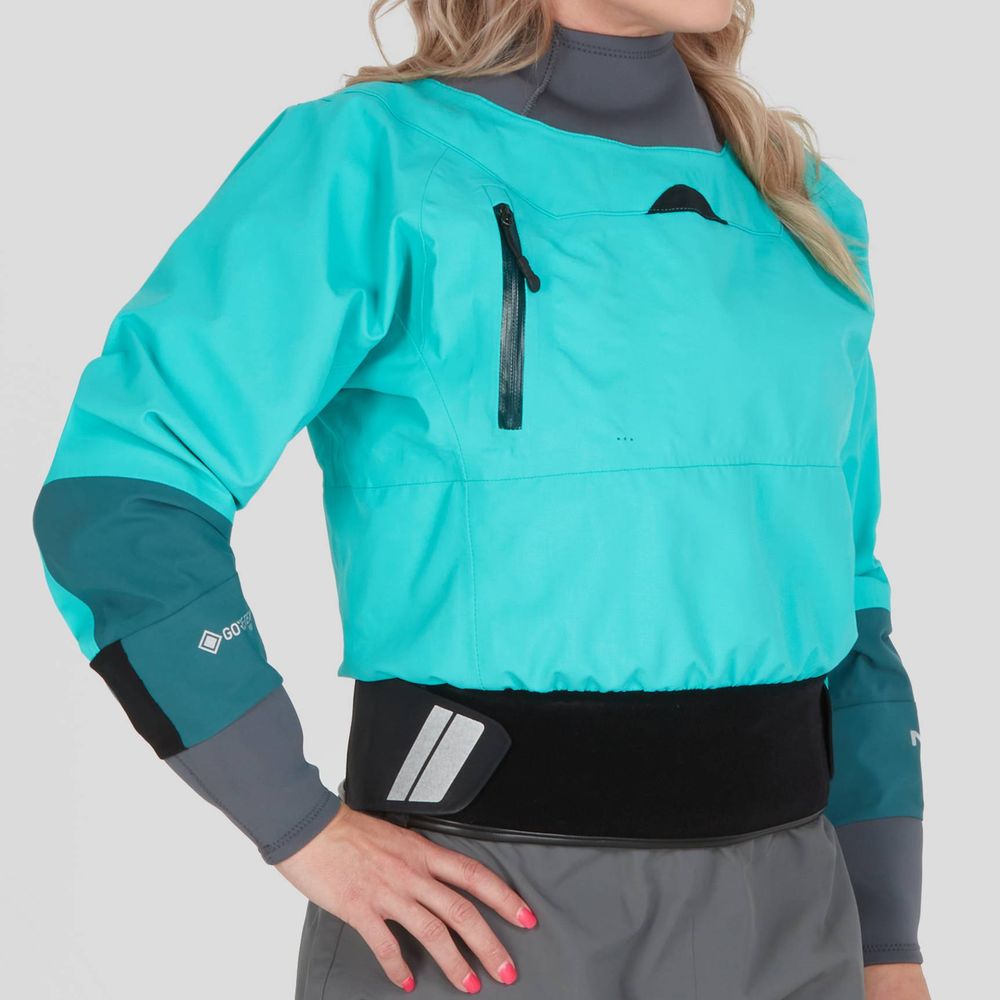 A woman models the NRS REV Drytop, showcasing its turquoise waterproof and breathable GORE-TEX Pro fabric with gray sleeves and black waist detail, as she places her hand on her hip.