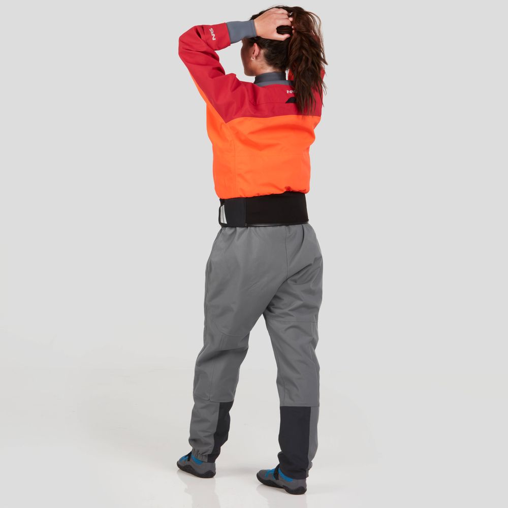 A person wears a vibrant red and orange NRS REV (GORE-TEX Pro) Drytop and gray pants, adjusting their hair against a plain light background.