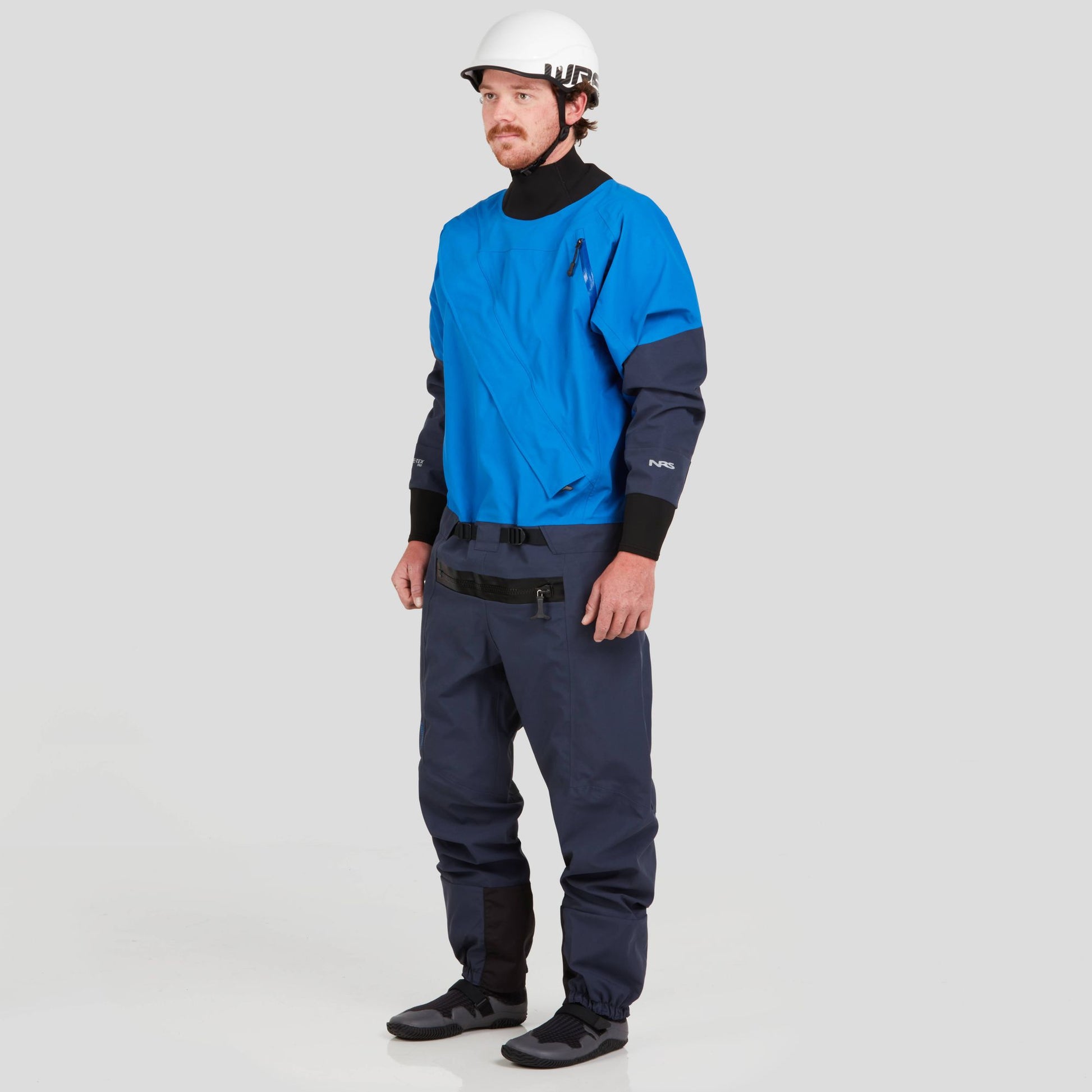 A person wearing the NRS Men's Nomad GORE-TEX Pro Semi-Dry Suit, which includes a blue top, black pants, a white helmet, and black shoes.