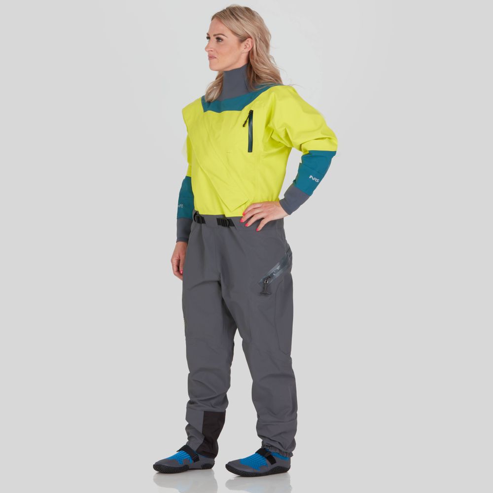 A person stands in the NRS Nomad GORE-TEX Pro Semi-Dry Suit for women, showcasing its waterproof performance with yellow and gray colors accented by blue, as they gaze to the side.