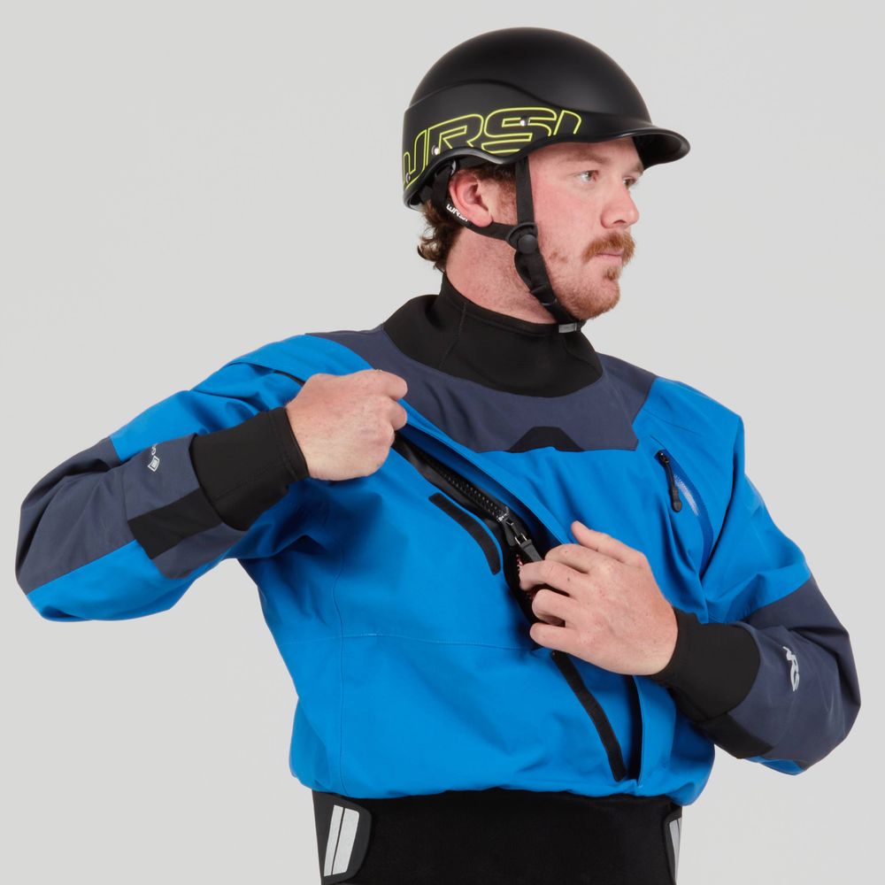 A person in a blue NRS Axiom (GORE-TEX Pro) dry suit made with recycled nylon and a black helmet adjusts the chest zipper.