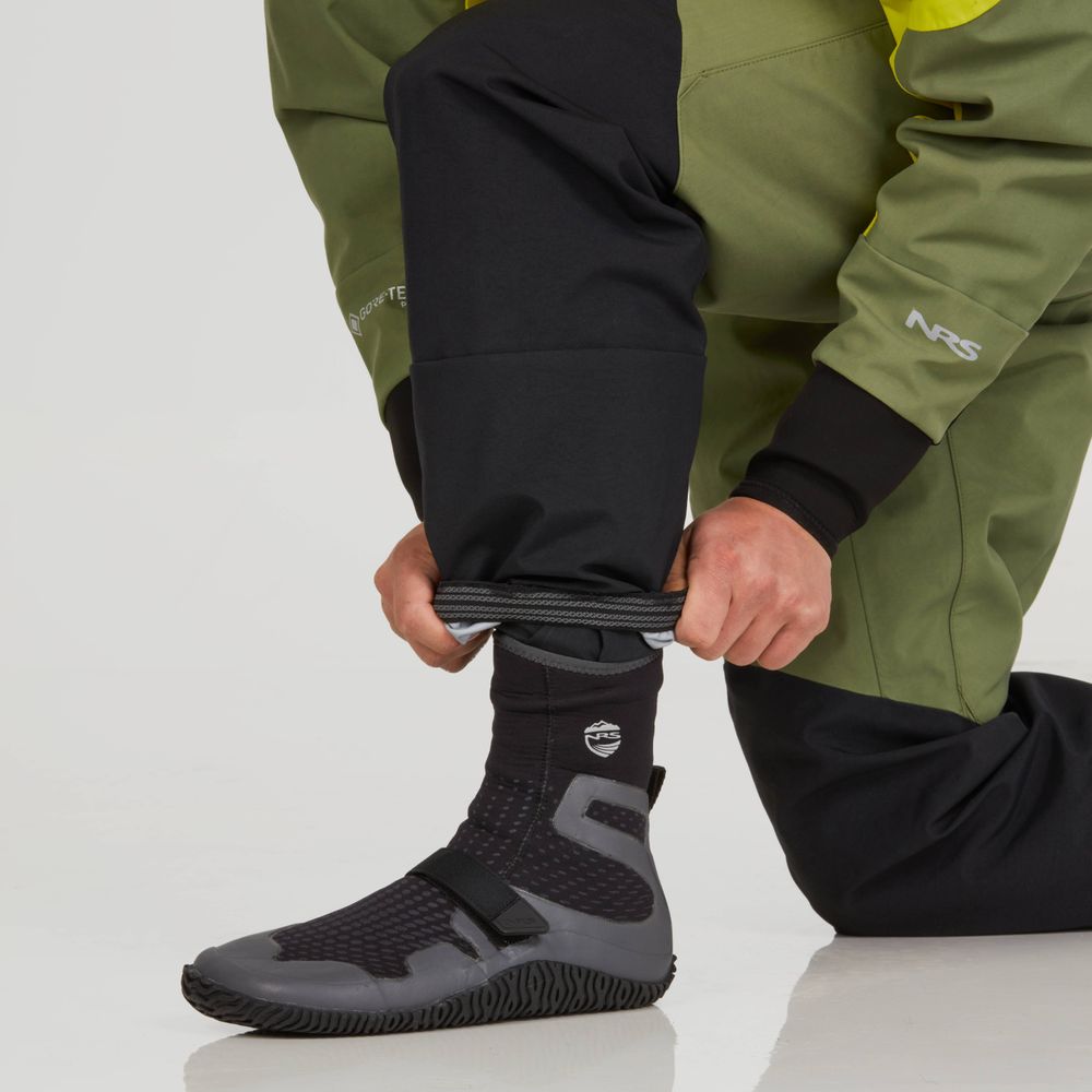 A person in a green and black NRS Axiom (GORE-TEX Pro) Drysuit - Men's adjusts their pant leg over a black and gray boot with a textured sole, expertly crafted from recycled nylon fabric.