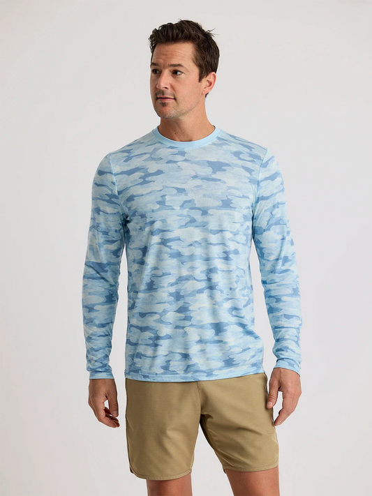 A man in a buttery-soft Free Fly Men's Bamboo Lightweight Long Sleeve camouflage shirt and khaki shorts stands against a plain light background.