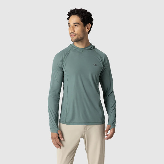 A man stands against a plain light gray background wearing the Outdoor Research Echo Hoodie - Men's in light teal (UPF 15) and beige pants.