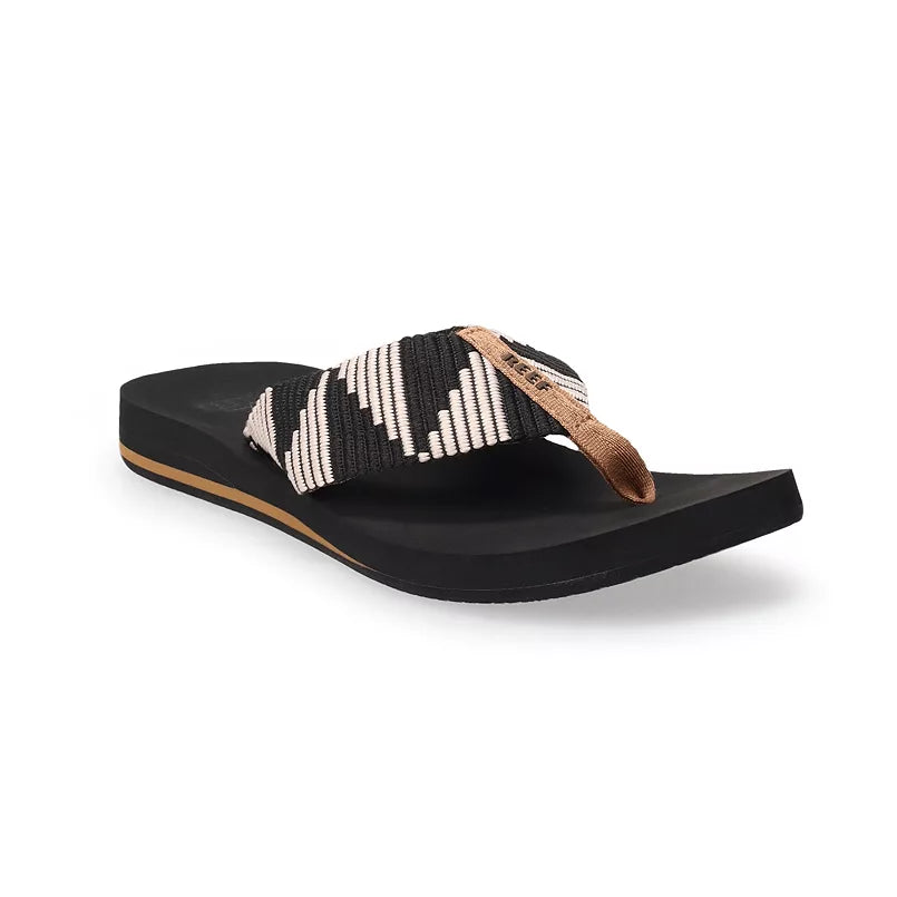 The REEF Spring Woven Reef Flip Flops feature a black sole, earth-friendly curved footbed, and a slight platform, with recycled plastic bottle straps in woven black, white, and tan.