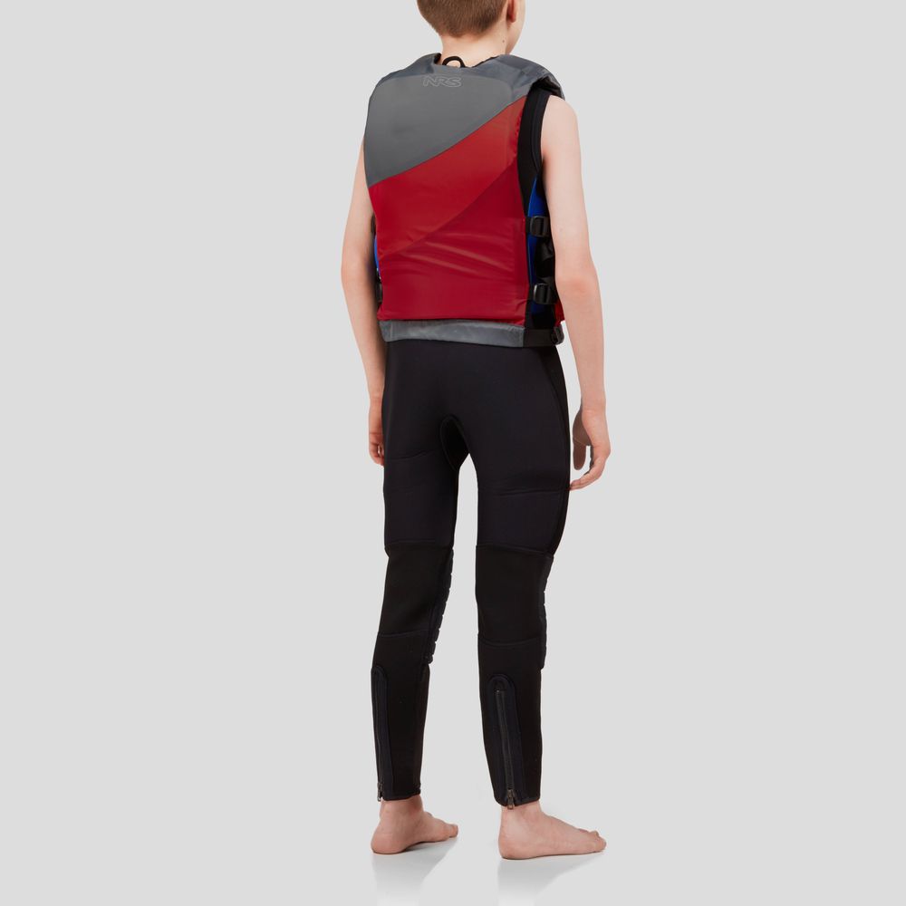 A person stands barefoot in a red and gray NRS Crew Youth PFD life jacket with US Coast Guard Type III Certification, wearing a black wetsuit. They are set against a plain gray backdrop, facing away from the camera.