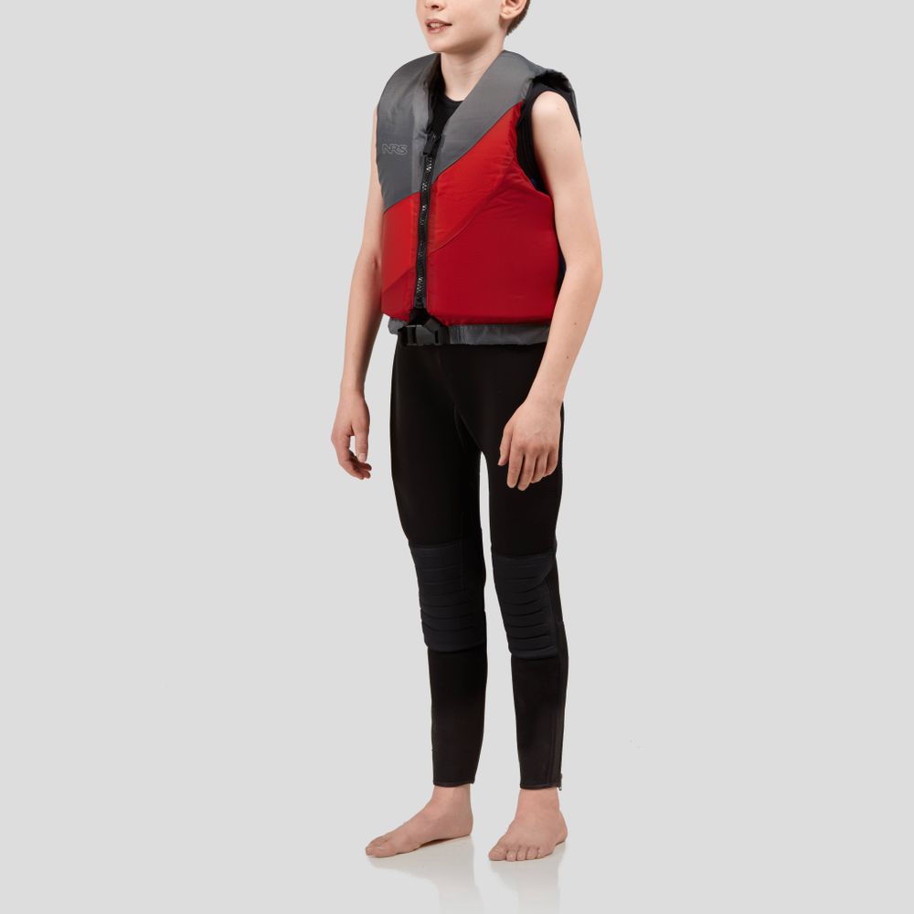 A child stands barefoot in an NRS Crew Youth PFD, a red and black US Coast Guard Type III Certified life jacket, over a black wetsuit against a plain background.