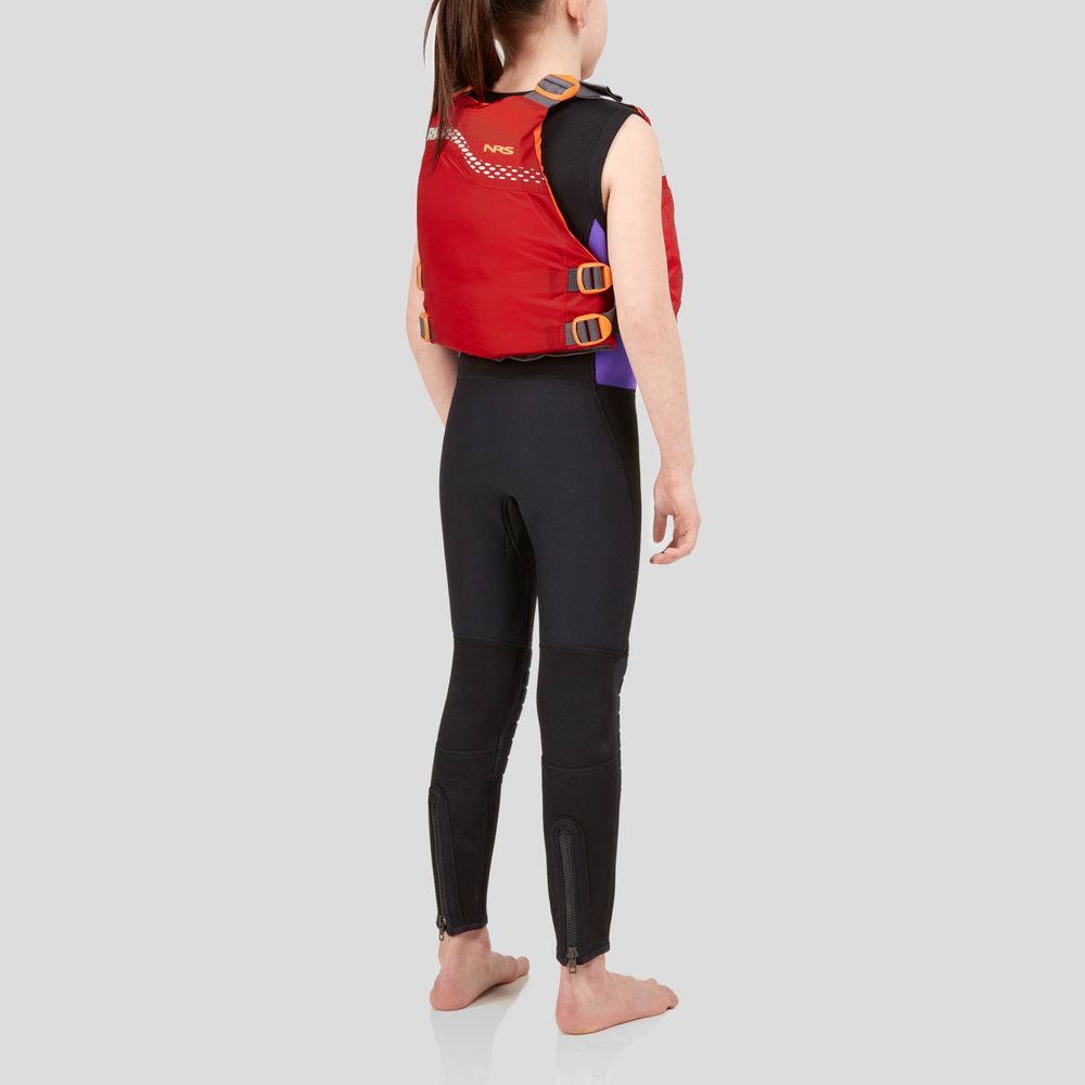 A person stands barefoot in a red NRS Vista Youth PFD life jacket and black wetsuit, set against a gray background, featuring Type III flotation.