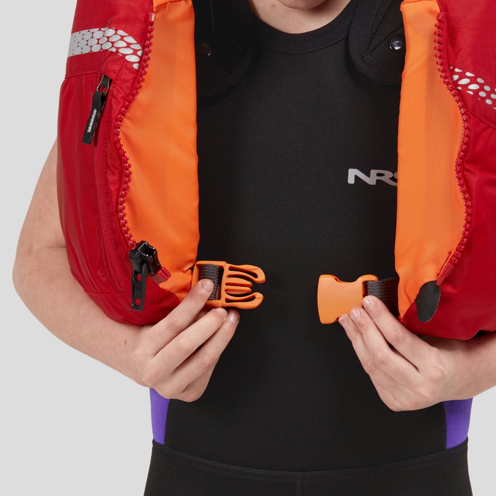 Wearing a sleek black wetsuit, a person fastens an orange buckle on the vibrant red and orange NRS Vista Youth PFD, crafted from durable 400 denier nylon.