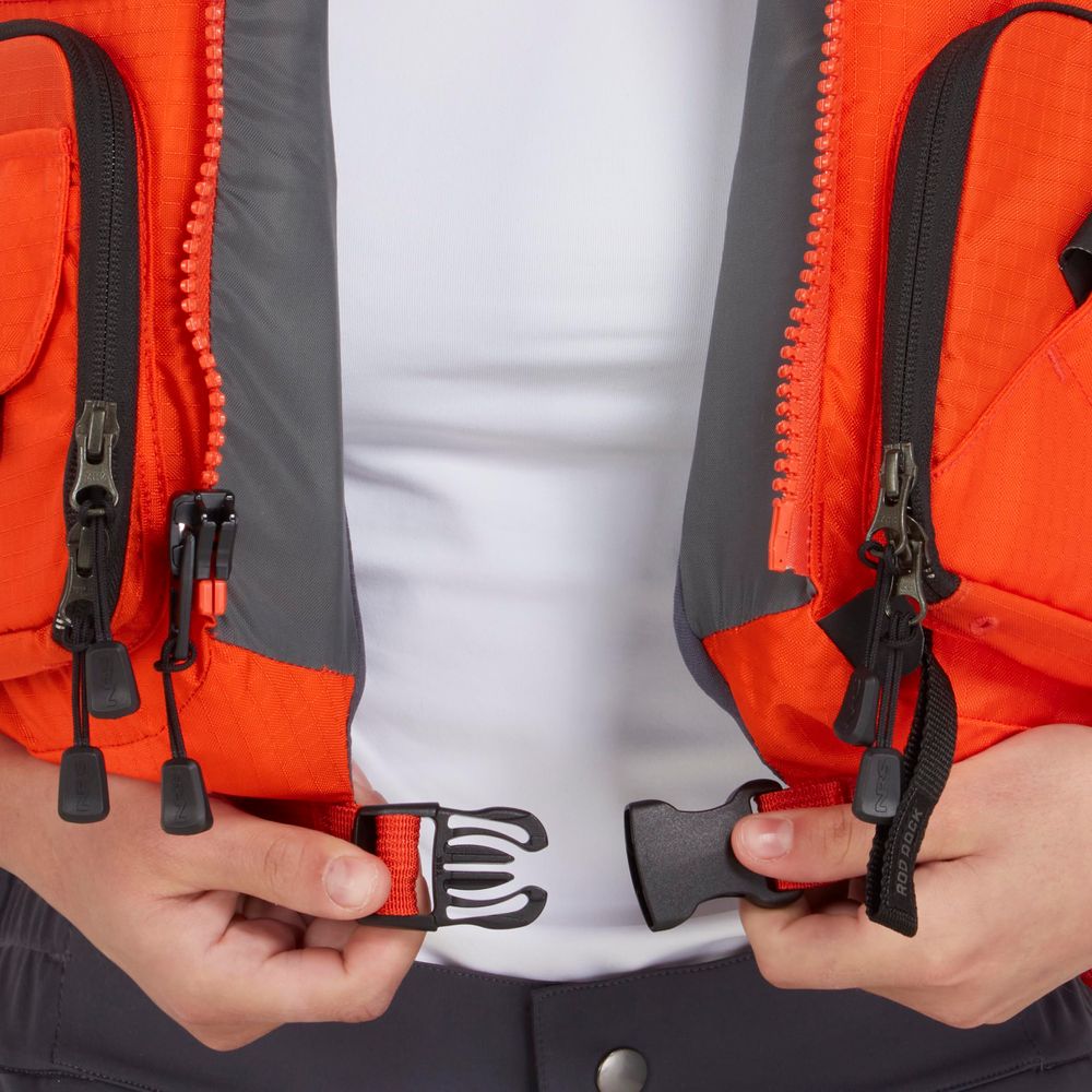 A person wearing the NRS Chinook Fishing PFD, an orange and gray life vest, fastens the black front buckle with both hands.