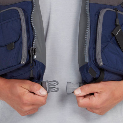 A person fastens the buckle of an NRS Chinook Fishing PFD, a blue and gray life vest with zippered pockets ideal for fishing outings.