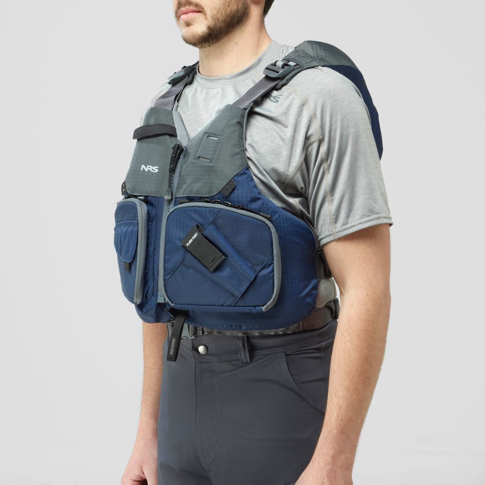 A man in a gray shirt and pants is wearing the NRS Chinook Fishing PFD, a blue and gray life jacket featuring multiple pockets and attachment points.