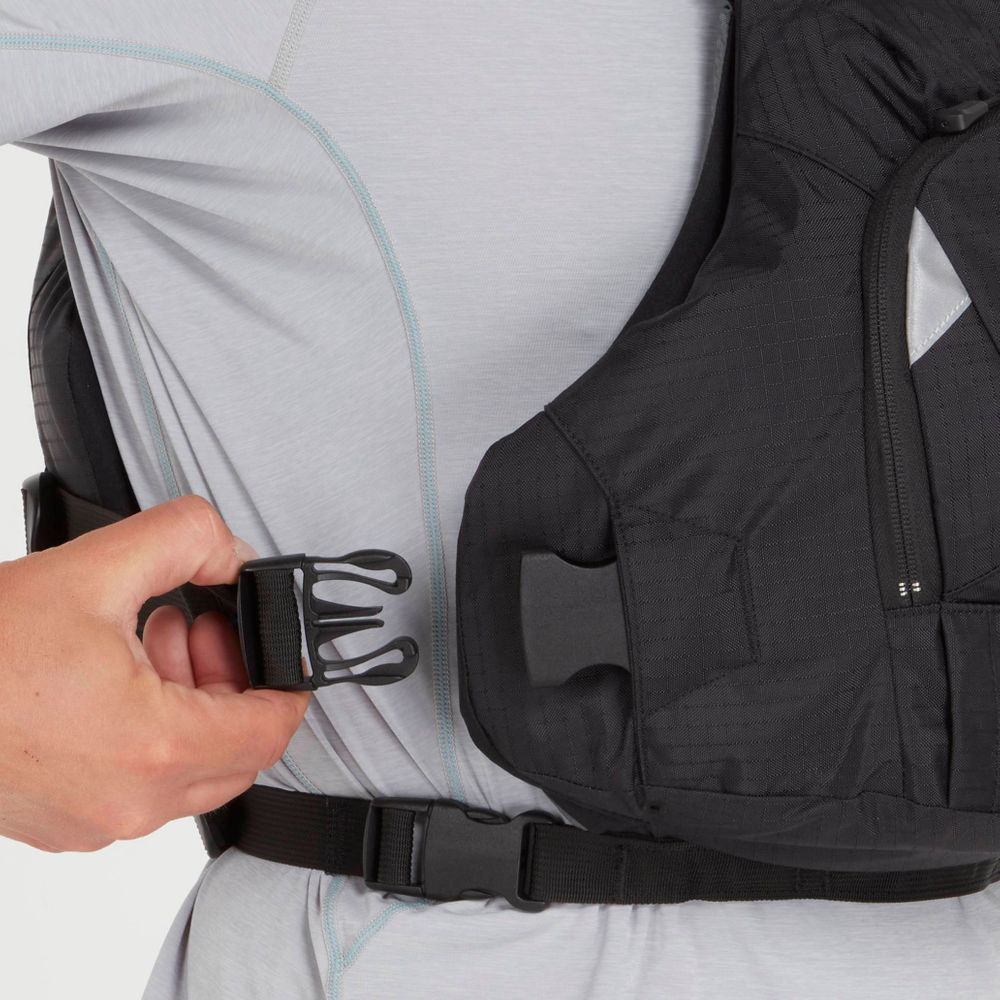 A person fastens a black buckle on a black padded vest similar to the NRS Ninja PFD, worn over a light gray long-sleeve shirt.