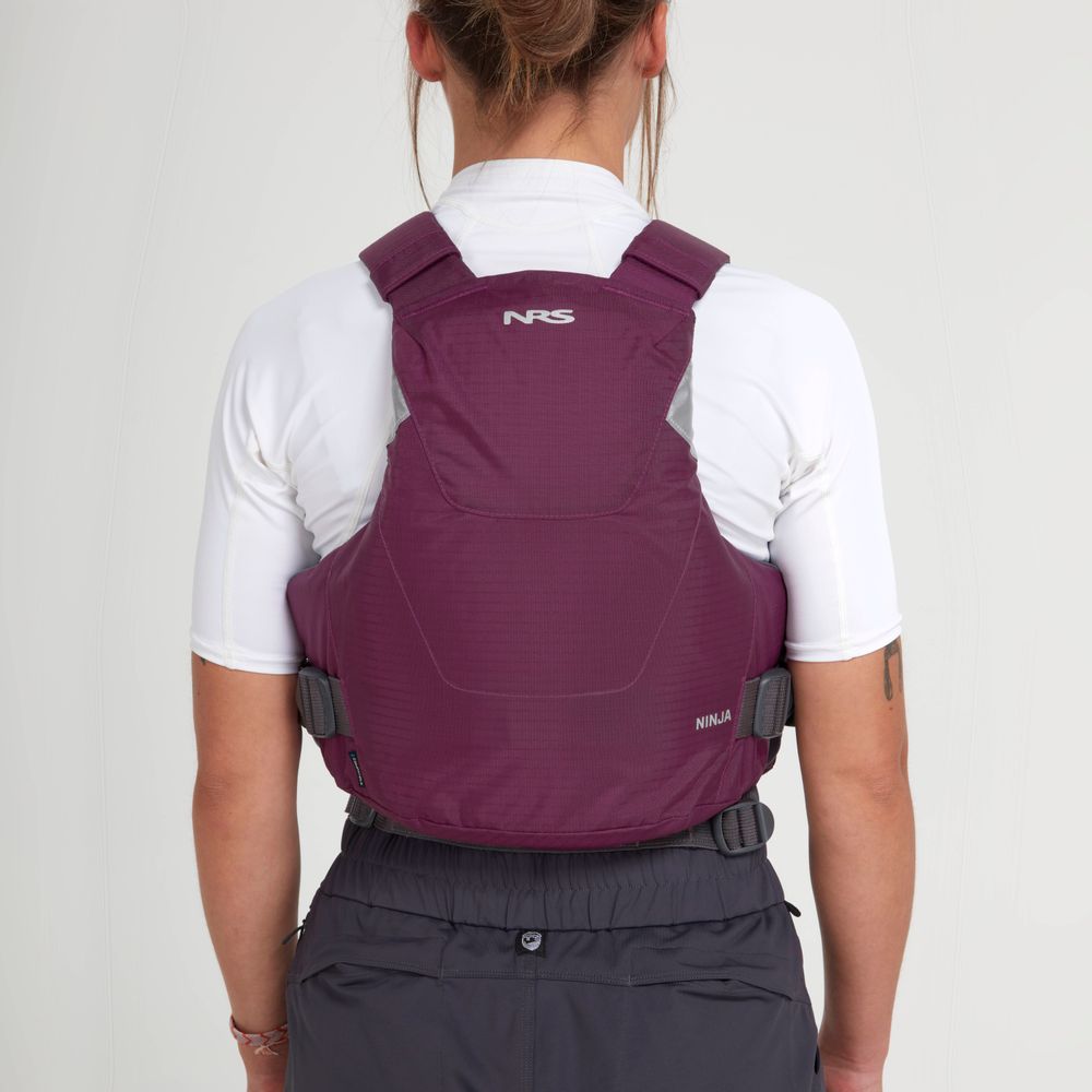 A person is seen from behind wearing an NRS Ninja PFD in purple over a white shirt and gray pants, highlighting compact flotation features.