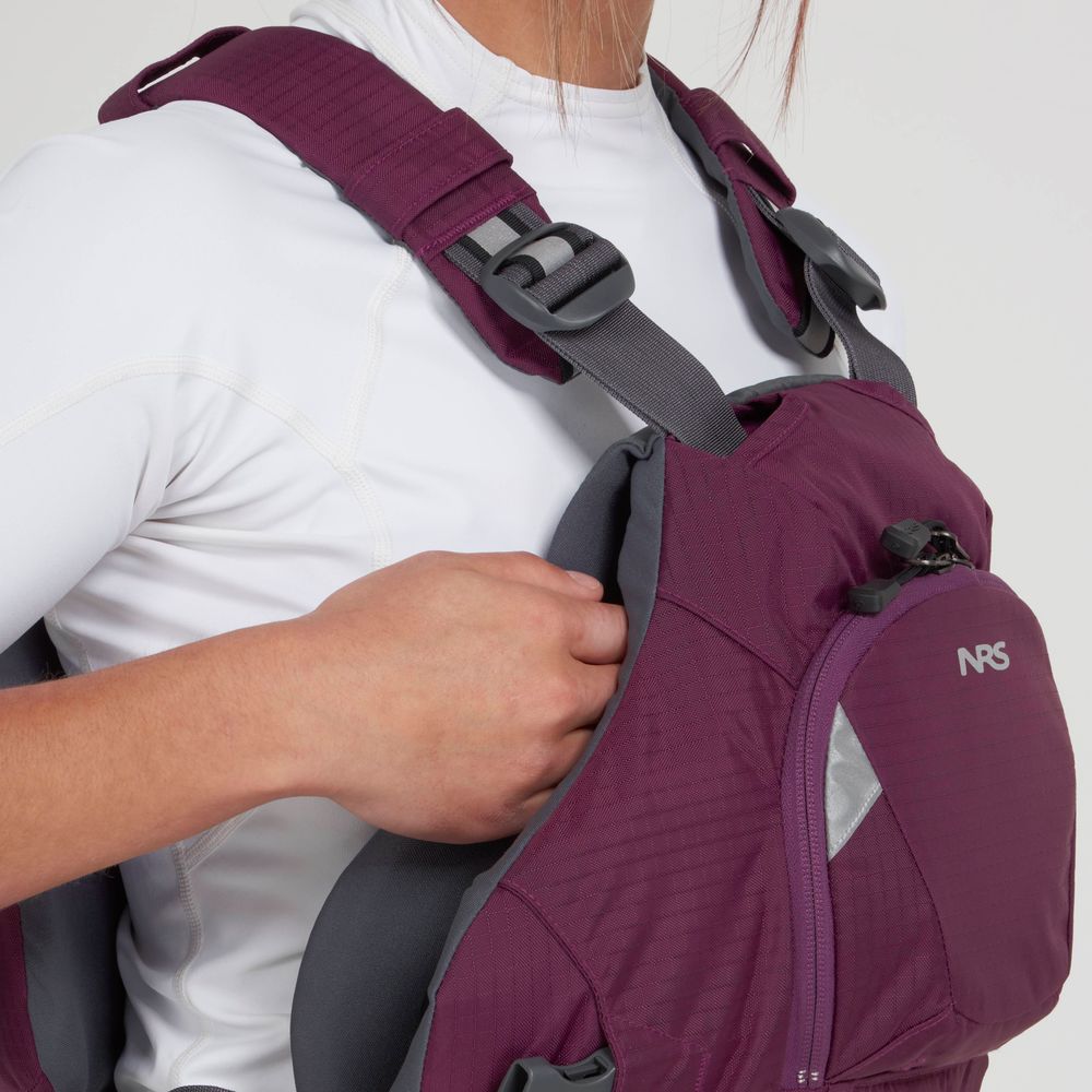 A person in a white top adjusts their NRS Ninja PFD with black straps, ensuring the maroon flotation device fits snugly for optimal performance.
