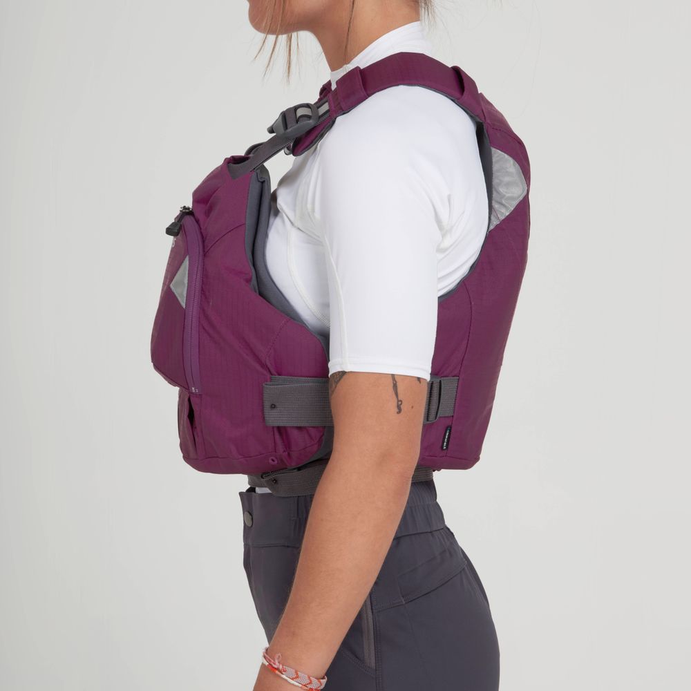 The person, wearing a maroon NRS Ninja PFD over a white shirt and gray pants, stands sideways with an air of readiness.