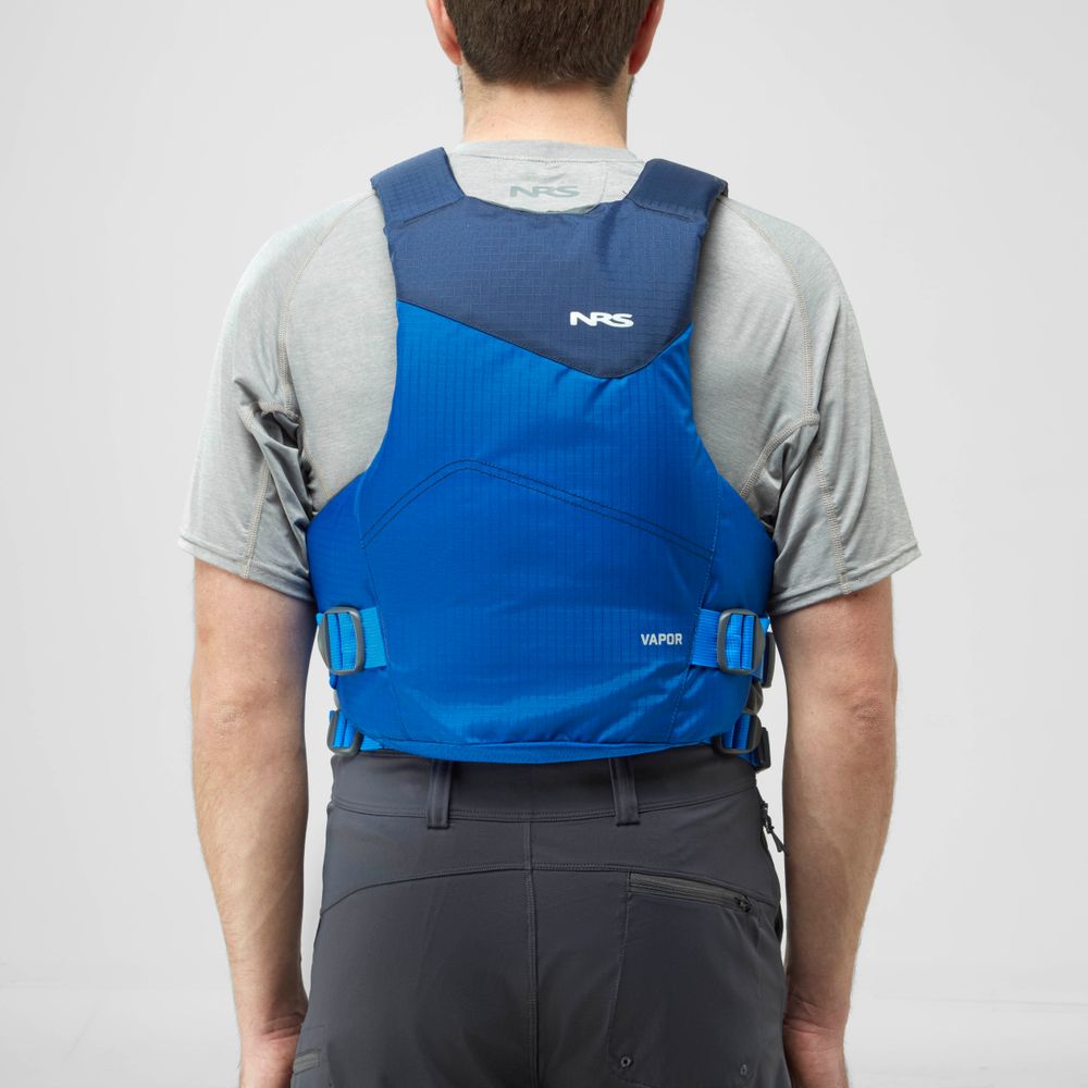 A person, seen from the back and ready to paddle, wears a blue NRS Vapor PFD over a gray t-shirt.