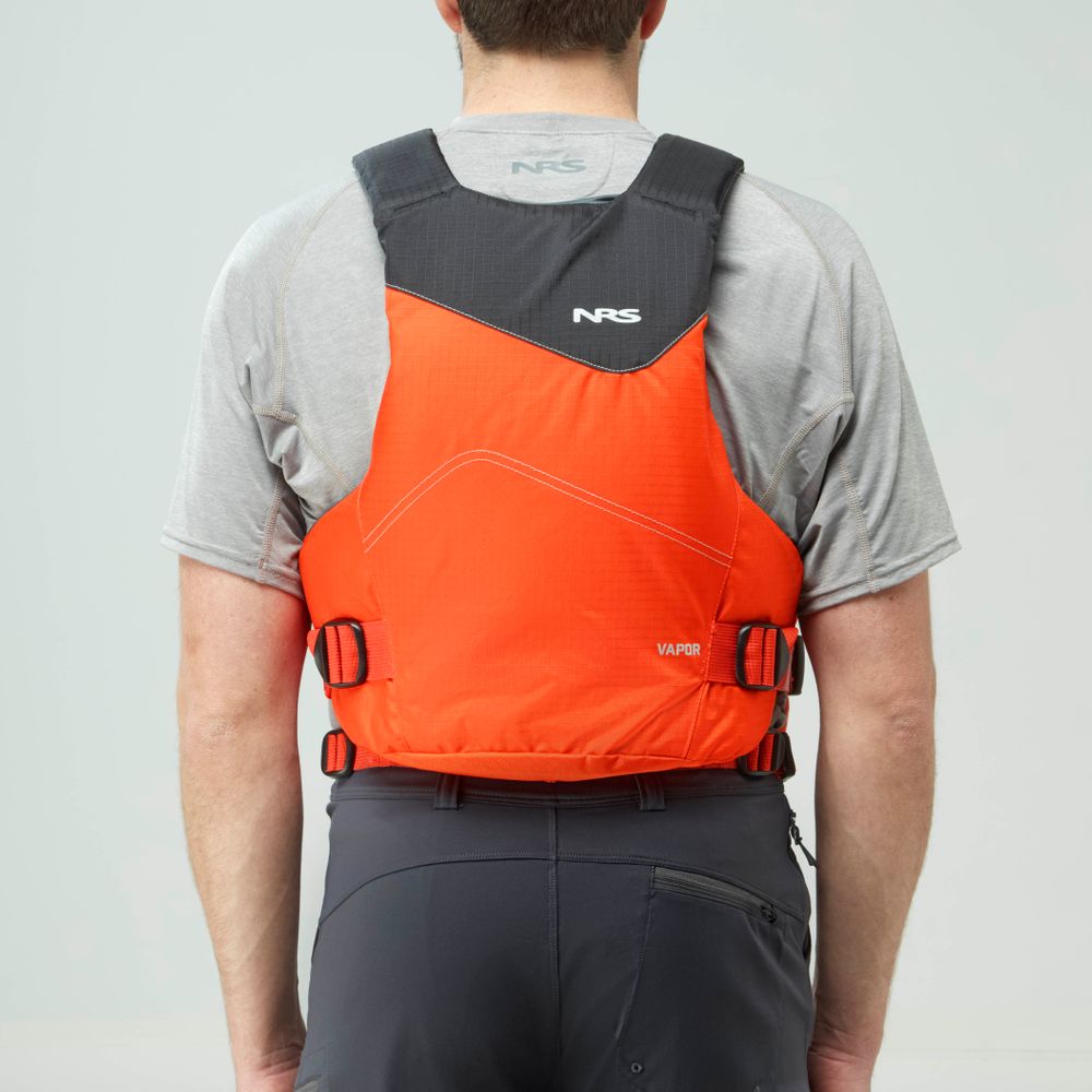 A person wearing a grey shirt and dark pants is seen from behind, paddling while wearing an orange NRS Vapor PFD with black straps.