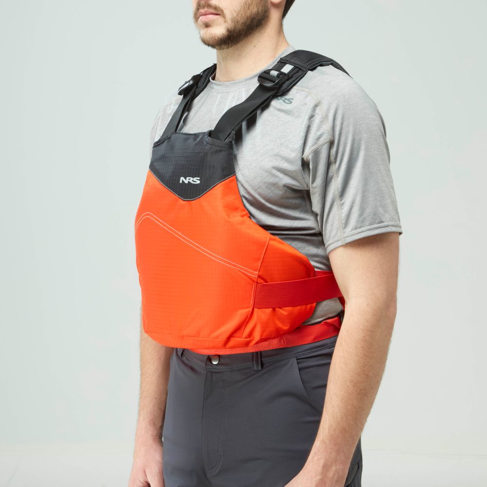 A man in a grey shirt and dark pants models the NRS Vapor PFD, an orange and black life jacket perfect for paddling, against a plain background.