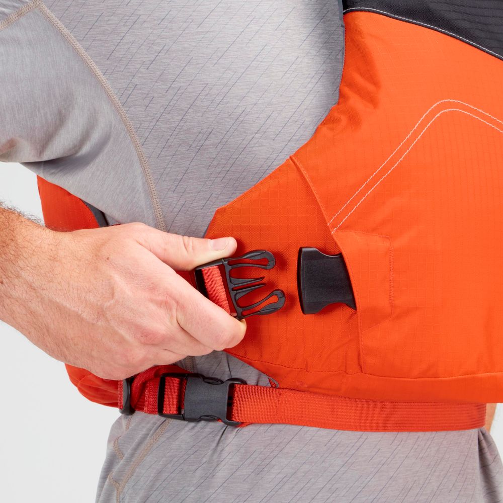 A person secures the side buckle of an orange NRS Vapor PFD life jacket over a gray shirt, getting ready to paddle.