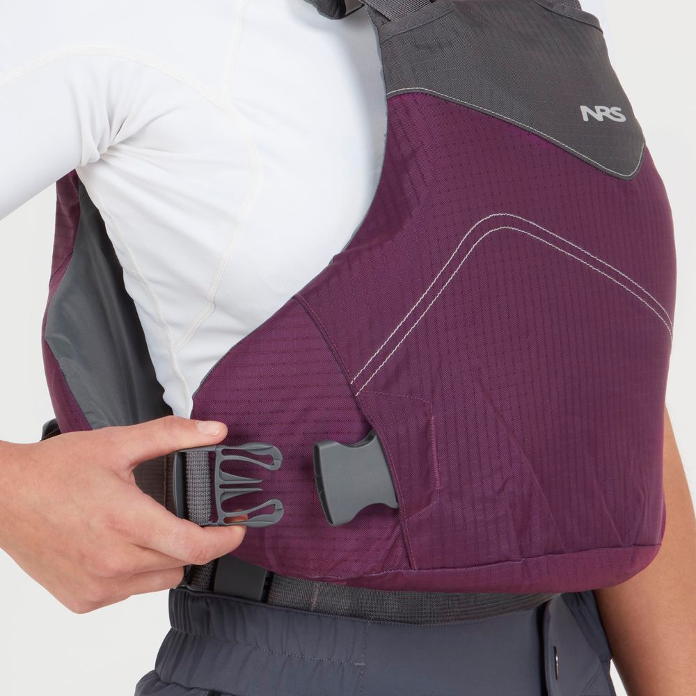 A person fastening the side buckle of an NRS Vapor PFD, dressed in a white long-sleeve shirt and dark pants—geared up for paddling adventures.