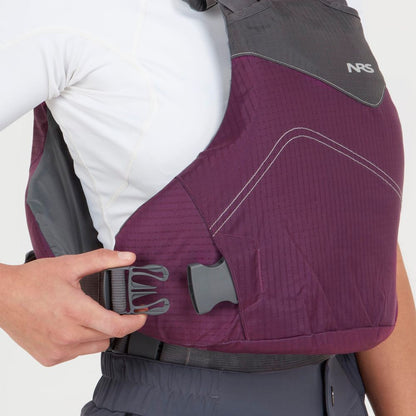 A person fastening the side buckle of an NRS Vapor PFD, dressed in a white long-sleeve shirt and dark pants—geared up for paddling adventures.