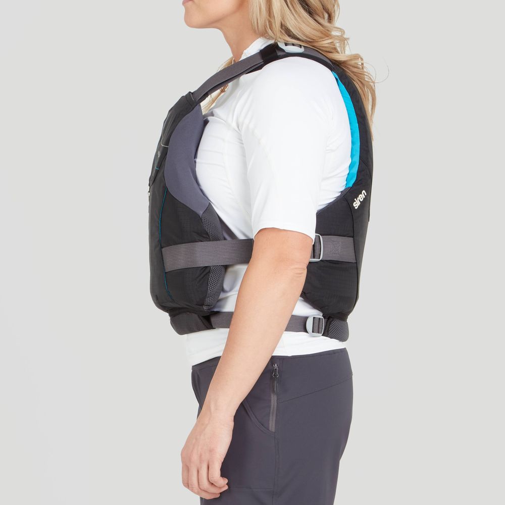 A woman wears the NRS Siren PFD in black and grey, showcasing its ultimate comfort and adjustable fit, over a white shirt and dark pants, standing in profile.