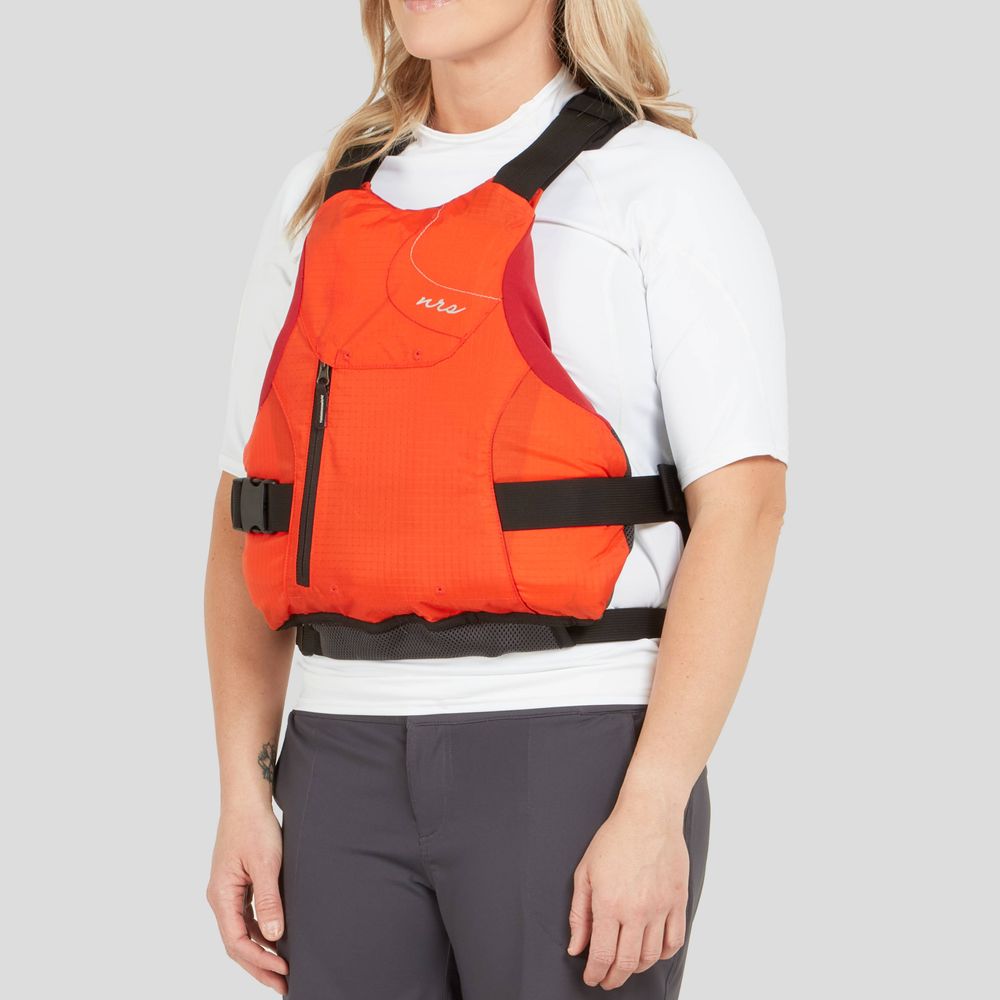 A woman stands in profile, donning the NRS Siren PFD over a white shirt. This bright orange life vest offers an adjustable fit for comfort, making it practical and stylish.