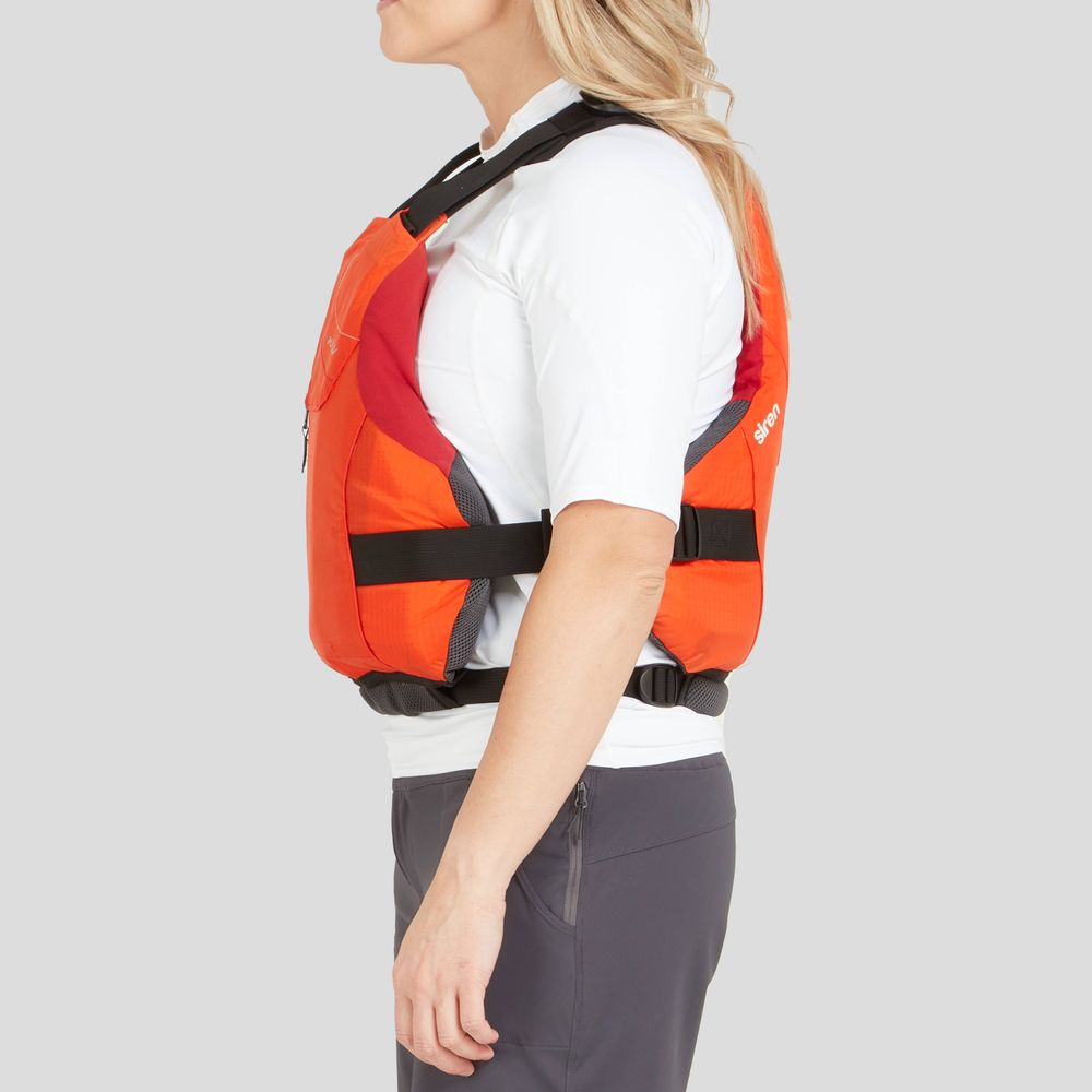 A woman in the NRS Siren PFD, an orange adjustable life vest, stands confidently in profile over a white shirt and dark pants against a plain background.