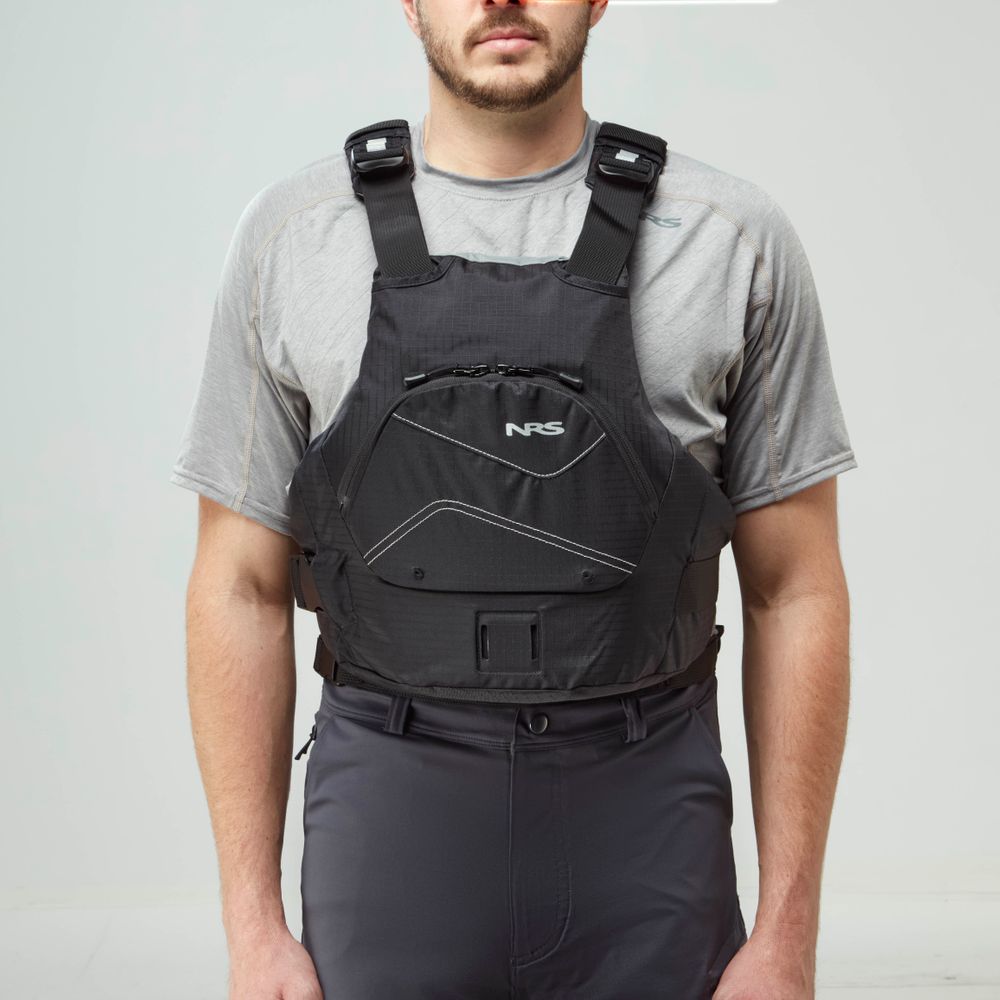 A person models the NRS Ion PFD, a black life jacket with US Coast Guard Certification, over a gray short-sleeve shirt and dark pants against a plain light background.