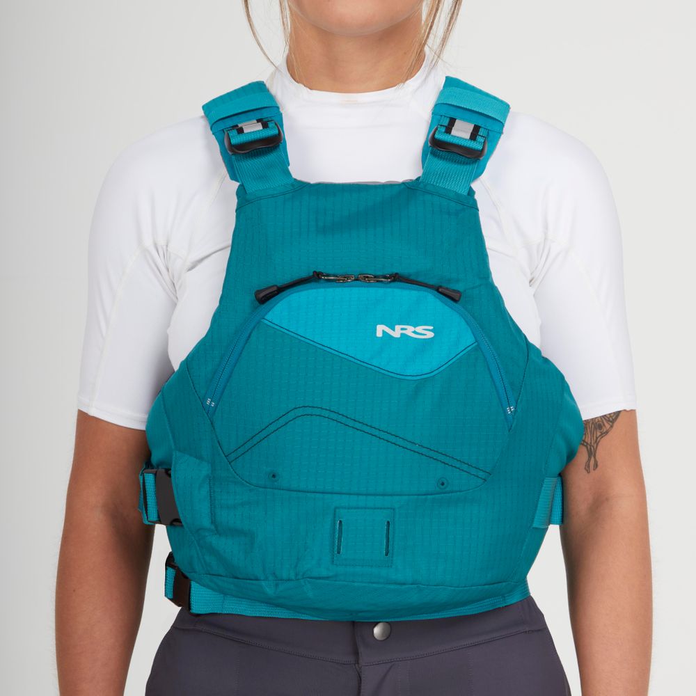 Someone wears the turquoise NRS Ion PFD (Type III), layered over a white short-sleeve shirt and dark pants, shown from shoulders to waist against a plain background.